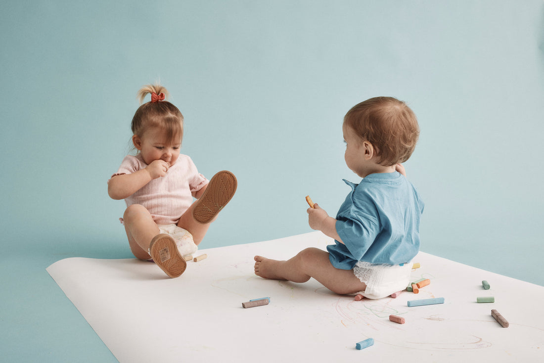 Två bebisar leker med kritor i Bammies bambublöjor – mjuk och skonsam passform för aktiva bebisar och toddlers.