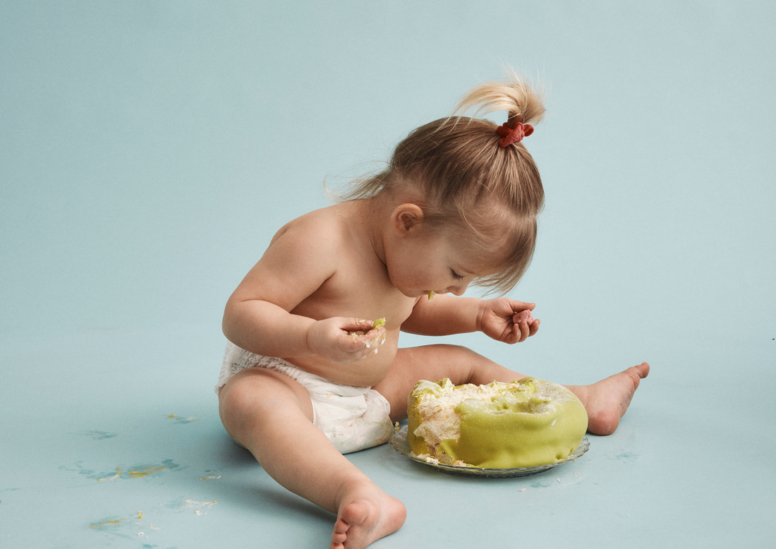 Ettårig bebis i Bammies blöja äter tårta i cake smash-fotografering