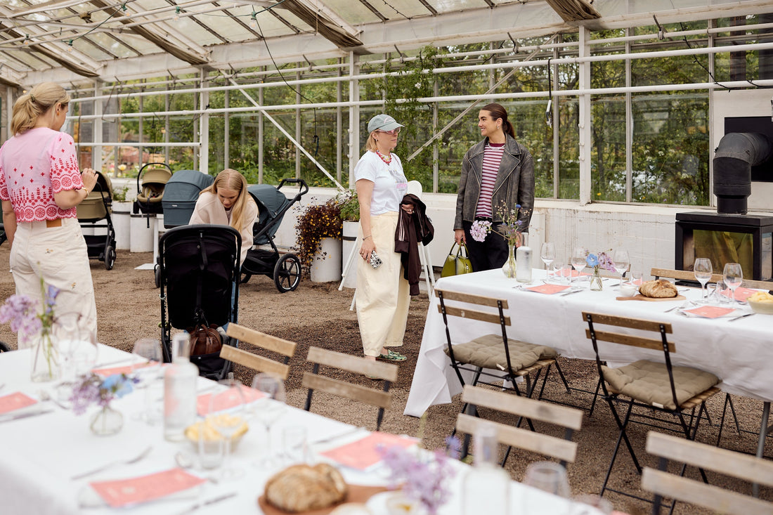 Gäster med barnvagnar minglar vid dukade bord på Bammies event i växthus